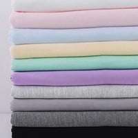 Une pile bien rangée de Jersey bambou uni avec élasthanne de Longan Craft France dans des couleurs unies douces - blanc, rose, jaune, vert menthe, violet, gris et noir - idéales pour des vêtements d'intérieur confortables.