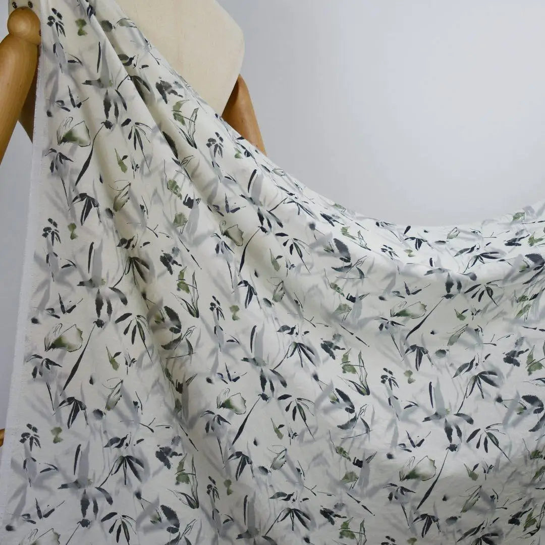 Un gros plan montre un mannequin portant du Tissu viscose imprimé bambou au mètre de Longan Craft France, un tissu léger en viscose de style chinoiserie présentant un délicat motif de feuilles noires et vertes sur un blanc doux, idéal pour les robes.