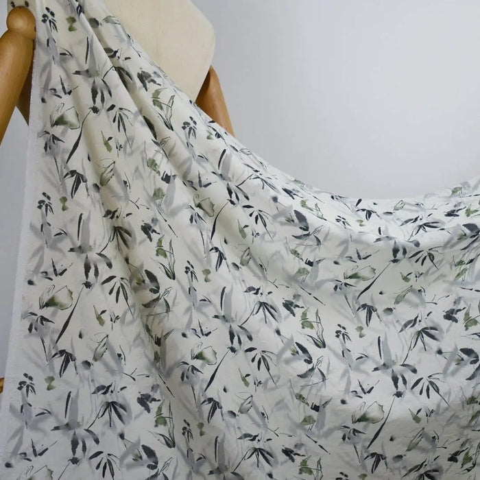 Un gros plan montre un mannequin portant du Tissu viscose imprimé bambou au mètre de Longan Craft France, un tissu léger en viscose de style chinoiserie présentant un délicat motif de feuilles noires et vertes sur un blanc doux, idéal pour les robes.