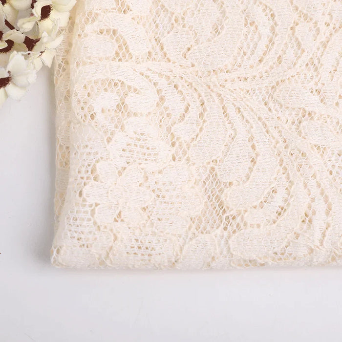 Un gros plan de la Dentelle florale beige au mètre de Longan Craft France montre son grand motif de dentelle florale, avec des fleurs blanches artificielles en haut à gauche, le tout sur un fond blanc uni. Dentelle idéale pour la couture.