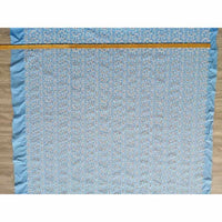 Un tissu brodé floral bleu en coton de Longan Craft France est posé à plat sur du bois, avec un mètre le long du bord supérieur. Ce "tissu brodé floral ajouré bleu au mètre" est 100 % coton et présente un motif floral ajouré.