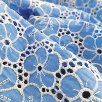 Gros plan sur le Tissu brodé floral ajouré bleu au mètre de Longan Craft France, un tissu 100% coton ajouré à base de bleu clair et de broderies florales blanches et bleu foncé, mettant en valeur les coutures détaillées et les motifs circulaires texturés.