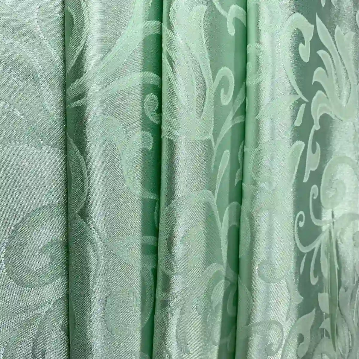 Gros plan sur le tissu damas brocart au mètre vert clair de Longan Craft France, un tissu jacquard brillant aux élégants motifs floraux et tourbillonnants, drapé en plis souples - idéal comme tissu pour rideaux en damas pour la décoration intérieure.