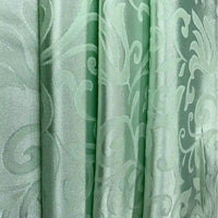 Gros plan sur le tissu damas brocart au mètre vert clair de Longan Craft France, un tissu jacquard brillant aux élégants motifs floraux et tourbillonnants, drapé en plis souples - idéal comme tissu pour rideaux en damas pour la décoration intérieure.