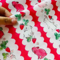 Une main tient le tissu de Pâques Longan Craft France motif lapin et carotte en coton, 100% doux et léger, parfait pour vos projets DIY de saison-un tissu imprimé adorable aux couleurs vives pour Pâques.