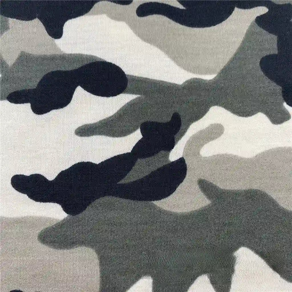 Gros plan sur le Tissu French Terry extensible imprimé camouflage au mètre de Longan Craft France, montrant des formes abstraites noires, grises et blanches qui se fondent les unes dans les autres - idéal pour les vêtements de sport respirants.