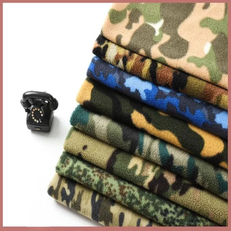Sept morceaux pliés de Tissu polaire camouflage au mètre de Longan Craft France sont empilés, montrant divers motifs brossés à double face. Un petit téléphone à cadran noir se trouve à gauche, le tout sur un fond blanc épuré.