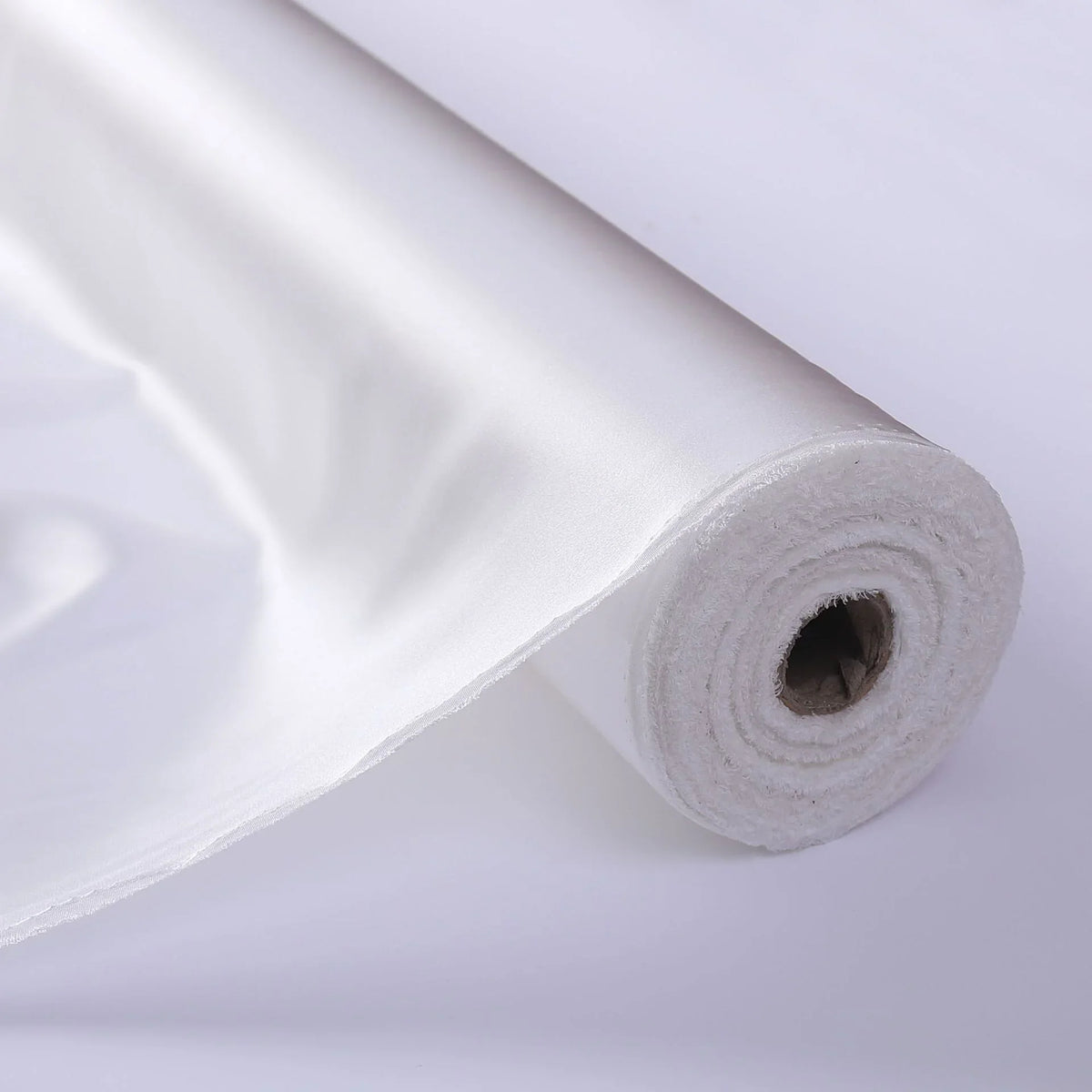 Gros plan sur le Tissu de soie charmeuse au mètre de Longan Craft France, déroulé pour révéler sa texture lisse et brillante de soie de mûrier, idéale pour les robes de mariée luxueuses.