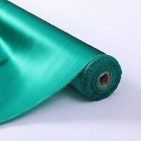 Un rouleau de Tissu de soie charmeuse au mètre de Longan Craft France, en soie de mûrier sarcelle brillante, est disposé avec le bord déroulé et le centre en carton visible - une luxueuse soie unie idéale pour les robes de mariée.