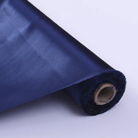 Un gros plan du Tissu de soie charmeuse au mètre de Longan Craft France en bleu foncé, partiellement déroulé, montre sa surface lisse et brillante et son cœur en carton sur un fond clair - idéal pour les robes de mariée luxueuses.