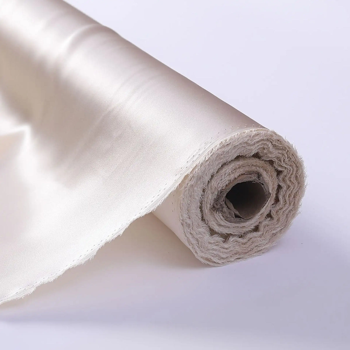 Gros plan d'un rouleau de tissu de soie charmeuse au mètre de Longan Craft France, un luxueux tissu de soie de mûrier blanc cassé destiné aux robes de mariée, dont l'une des extrémités laisse apparaître les couches internes et l'âme en carton, sur fond blanc.
