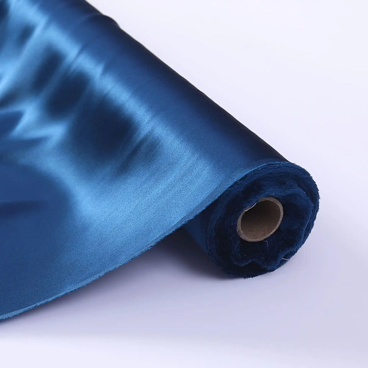 Un rouleau de Tissu de soie charmeuse au mètre de Longan Craft France, une soie Mulberry d'un bleu lustré parfaite pour les robes de mariée, est partiellement déroulé sur une surface blanche, montrant sa texture lisse et réfléchissante et son cœur en carton brun.