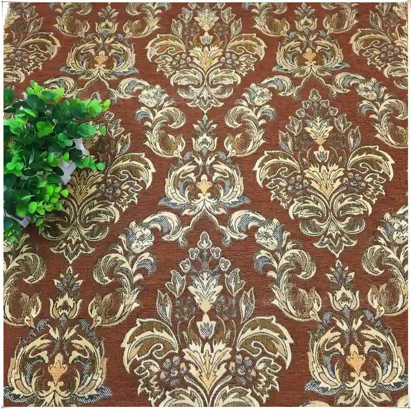 Gros plan sur le tissu d'ameublement damassé chenille à motif floral de Longan Craft France, présentant des motifs bruns et dorés ornés, avec une petite plante verte en pot dans le coin supérieur gauche.