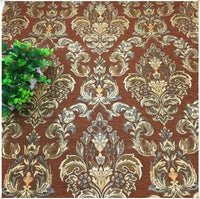 Gros plan sur le tissu d'ameublement damassé chenille à motif floral de Longan Craft France, présentant des motifs bruns et dorés ornés, avec une petite plante verte en pot dans le coin supérieur gauche.