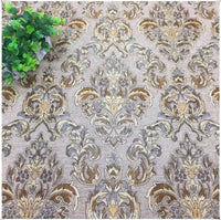 Une partie du tissu damassé jacquard à motifs floraux de Longan Craft France, présentant un fond beige avec un motif floral complexe brun et or, est représentée avec une petite plante verte artificielle dans le coin supérieur gauche.