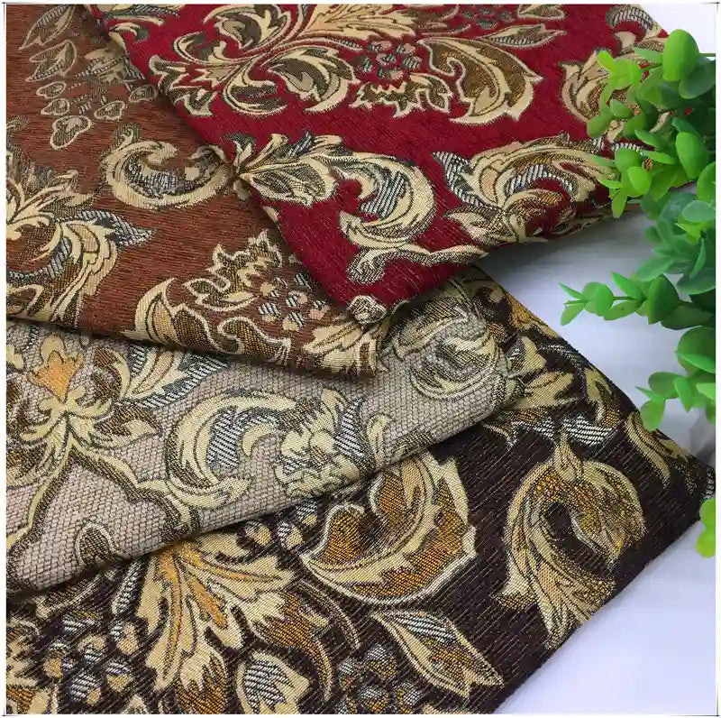 Trois pièces pliées en tissu damassé jacquard à motifs floraux rouge, marron, beige et or de Longan Craft France sont empilées à côté d'une petite plante verte en pot.