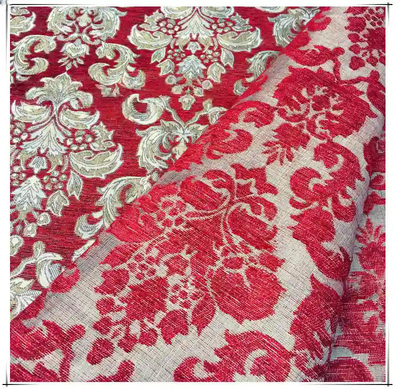 Gros plan sur le tissu damassé chenille au mètre de Longan Craft France, un jacquard d'ameublement aux motifs floraux ornés de rouge et d'or. Un coin est plié pour révéler le motif complexe au verso.