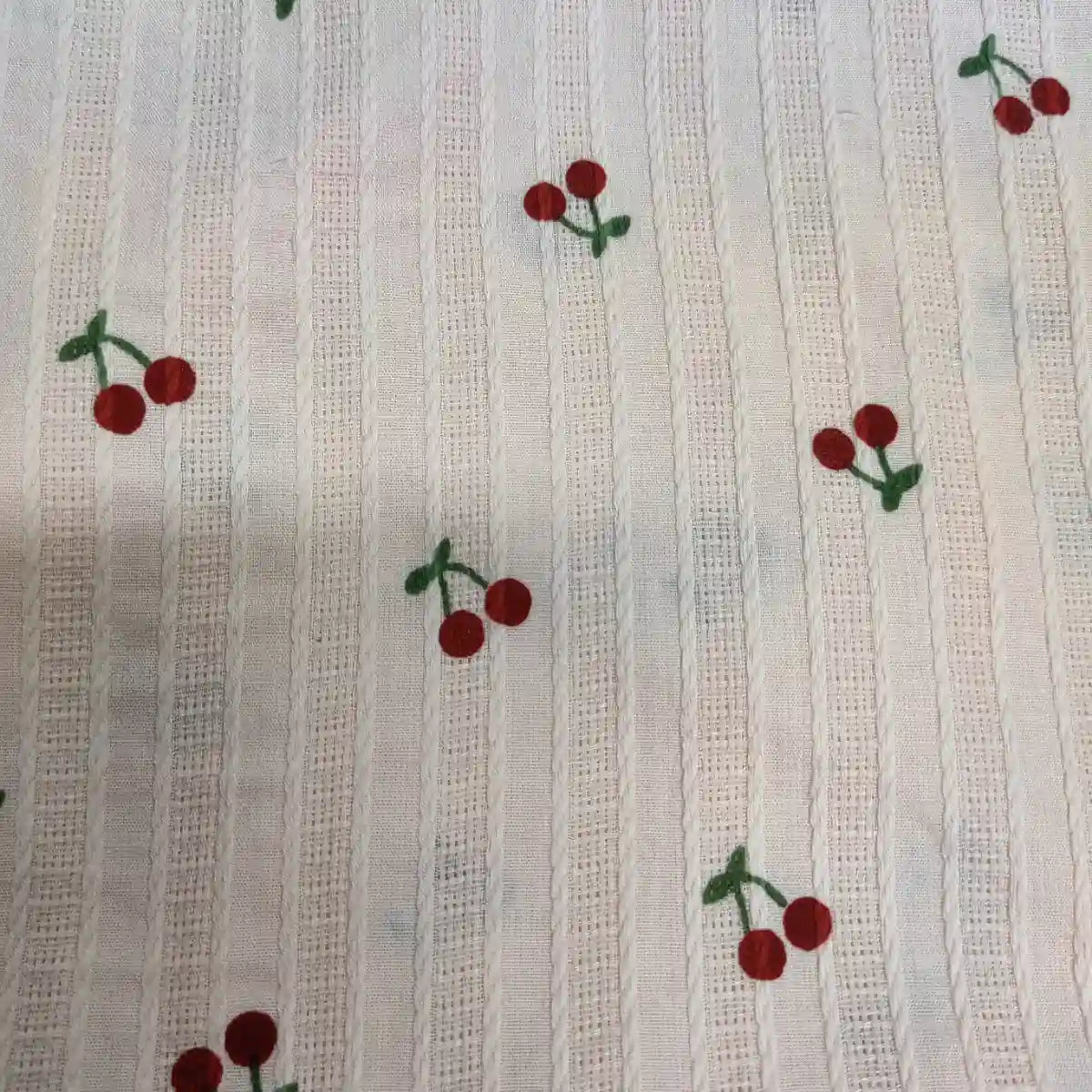 Tissu dobby texturé imprimé cerises au mètre de Longan Craft France : coton confortable avec motif rayé vertical, parsemé de petites cerises rouges à tiges vertes. Idéal pour vêtements, vendu au mètre.