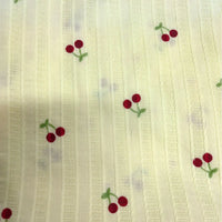 Tissu dobby texturé imprimé cerises au mètre de Longan Craft France : coton léger crème à rayures, décoré de petits motifs de paires de cerises rouges aux tiges vertes, idéal pour vêtements.