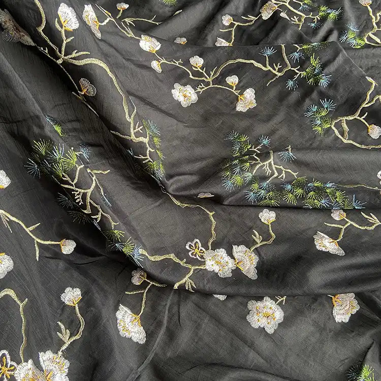 Gros plan sur le tissu de coton et de soie de mûrier de Longan Craft France, de style chinoiserie, qui présente des motifs floraux et des branches brodées en blanc, jaune et vert, avec des coutures détaillées et une texture luxueuse.