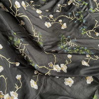 Gros plan sur le tissu de coton et de soie de mûrier de Longan Craft France, de style chinoiserie, qui présente des motifs floraux et des branches brodées en blanc, jaune et vert, avec des coutures détaillées et une texture luxueuse.