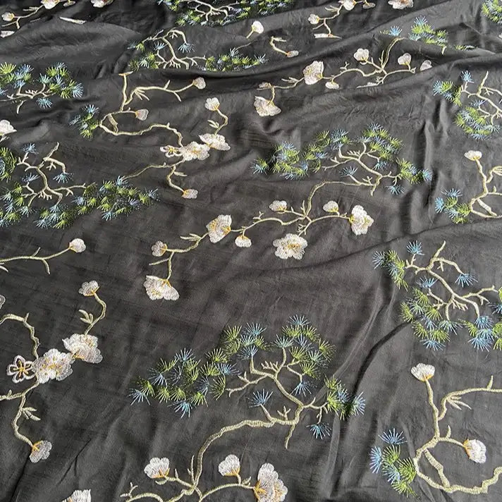 Le tissu coton et soie brodé de style chinois de Longan Craft France est orné de branches d'arbres, de fleurs blanches et d'aiguilles vertes pour un motif botanique élégant, idéal pour chemisiers ou projets haut de gamme.