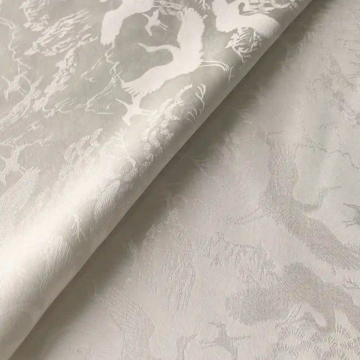 Gros plan sur le Tissu chinois en polyester-viscose au mètre de Longan Craft France, qui présente un jacquard botanique pâle et brillant avec un subtil motif floral en relief - idéal pour les rideaux - représenté avec un bord plié.