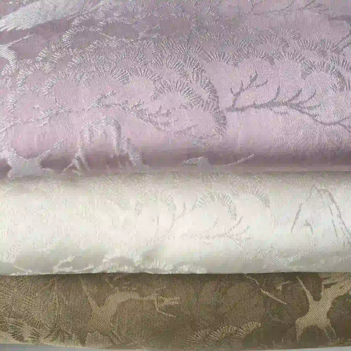 Trois rouleaux de tissu chinois en polyester-viscose de Longan Craft France, en violet clair, blanc cassé et beige avec des motifs botaniques jacquard - des tissus en viscose parfaits pour des rideaux ou un décor élégant.