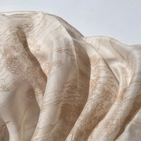 Gros plan sur le tissu en lyocell imprimé chinoiserie au mètre, beige clair, semi-transparent, de Longan Craft France, doucement drapé pour montrer son motif délicat et sa fluidité - idéal pour la couture.