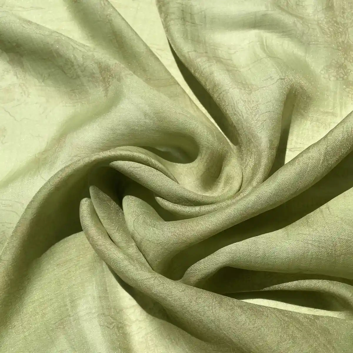 Un gros plan du Tissu en lyocell imprimé chinoiserie au mètre de Longan Craft France montre des plis doux, vert clair, avec une brillance subtile - parfait pour les robes grâce à sa matière lyocell légère et délicatement texturée.