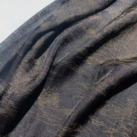 Un gros plan sur le tissu en lyocell imprimé chinoiserie au mètre de Longan Craft France montre une lumière douce sur les plis texturés, mettant en valeur le subtil motif doré chinois shanshui et le drapé doux et léger, idéal pour confectionner des robes.