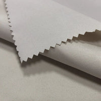 Gros plan sur le tissu peau de pêche imperméable enduit au mètre de Longan Craft France, un polyester microfibre à la texture douce et chaude, parfait pour les gilets. Des échantillons empilés montrent la surface lisse et résistante à l'eau du tissu blanc et son bord coupé en zigzag.