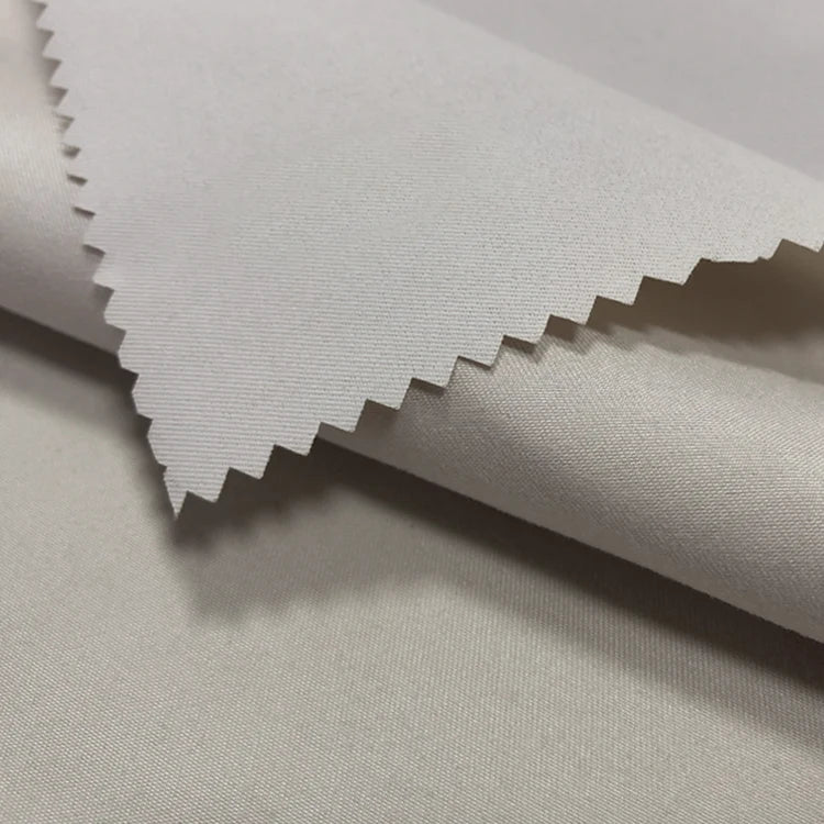 Gros plan sur le tissu peau de pêche imperméable enduit au mètre de Longan Craft France, un polyester microfibre à la texture douce et chaude, parfait pour les gilets. Des échantillons empilés montrent la surface lisse et résistante à l'eau du tissu blanc et son bord coupé en zigzag.