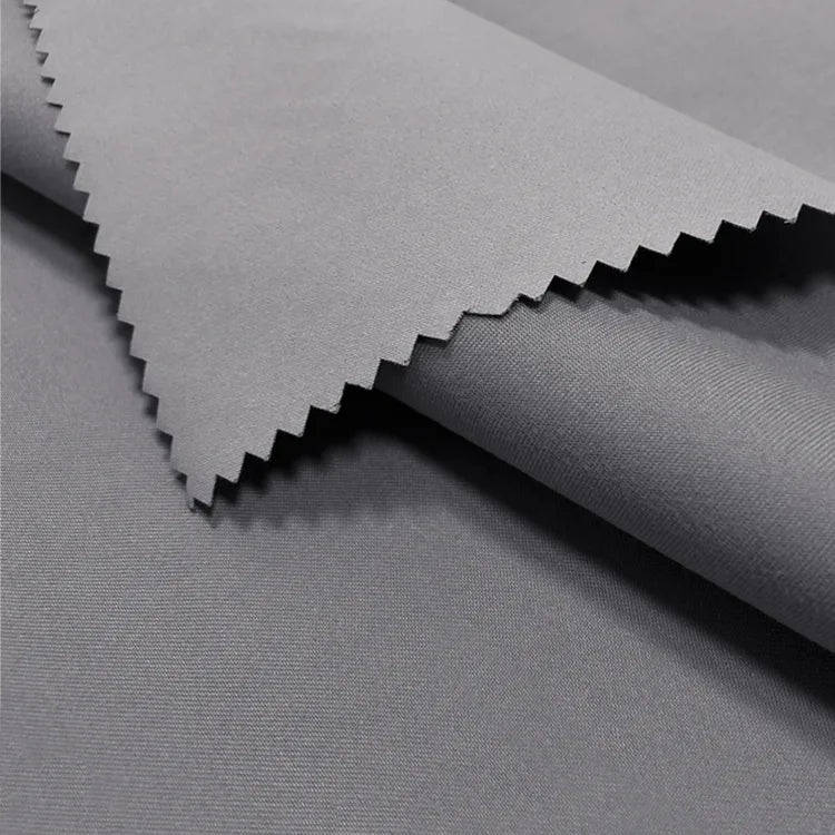 Deux pièces de tissu peau de pêche imperméable enduit au mètre de Longan Craft France - microfibre de polyester douce et chaude de couleur grise avec une finition mate - l'une avec un bord en zigzag et l'autre superposée sur une surface plane.