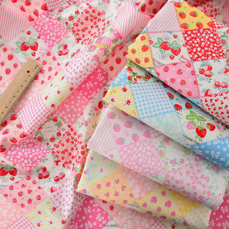 Le tissu popeline imprimée effet patchwork multicolore de Longan Craft France, aux motifs de fleurs et de fraises, est présenté avec une règle pour l'échelle - le tissu popeline idéal pour les projets de couture, le patchwork ou les vêtements.