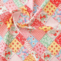 Gros plan sur le tissu popeline imprimé effet patchwork multicolore de Longan Craft France, qui présente des motifs floraux et de fraises dans des couleurs vives. Le tissu de coton destiné à l'habillement est légèrement froncé au centre.