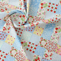 Gros plan sur la popeline imprimée effet patchwork multicolore de Longan Craft France, qui présente des motifs floraux et de fraises en bleu, jaune et blanc. Le tissu froncé présente des carrés vichy et à pois pour le patchwork ou la confection de vêtements.