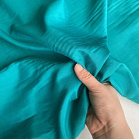 Une main tient un morceau de Soie de coton multicolore au mètre de Longan Craft France, montrant la texture lisse et les plis doux de ce tissu de doublure en soie léger et respirant.