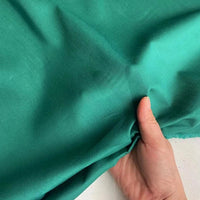 Une main tient et fronce légèrement un morceau de Soie de coton multicolore au mètre de Longan Craft France, un tissu léger en soie de mûrier qui met en valeur sa texture lisse et son drapé élégant.