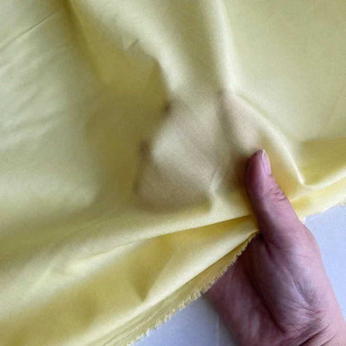 Une main soulève un morceau de Soie de coton multicolore au mètre - légère soie de mûrier de Longan Craft France - illustrant sa texture douce, sa légèreté et son aspect translucide, idéale en tissu de doublure en soie respirant.