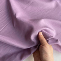 Une main saisit et froisse délicatement le Soie de coton multicolore au mètre de Longan Craft France, un tissu de doublure en soie de mûrier léger et respirant, mettant en valeur sa texture lisse et son toucher doux.
