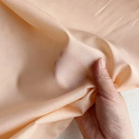 Une main pince et soulève le Soie de coton multicolore au mètre de Longan Craft France, un tissu de mûrier léger, doux et lisse avec une légère brillance - parfait comme doublure en soie respirante.