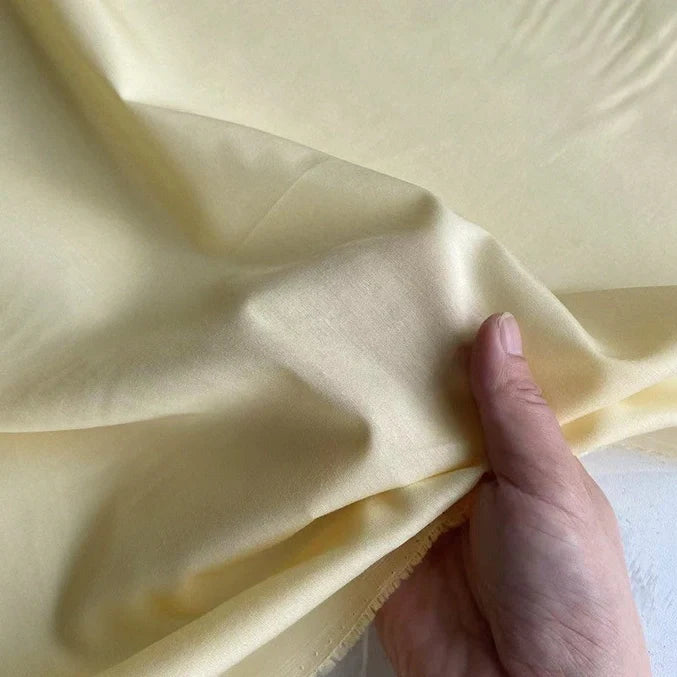 Une main soulève un morceau de soie de coton multicolore au mètre de Longan Craft France, mettant en valeur sa texture douce et légère et sa brillance subtile, idéale comme soie de mûrier doublure respirante.