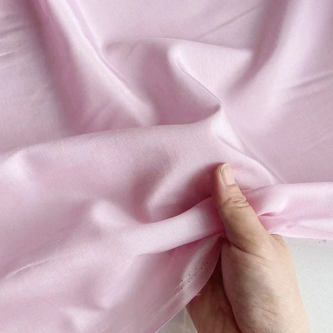 Une main tient et froisse doucement le Soie de coton multicolore au mètre de Longan Craft France, un tissu de doublure en soie de mûrier léger et respirant, révélant sa texture lisse et sa douceur luxueuse.