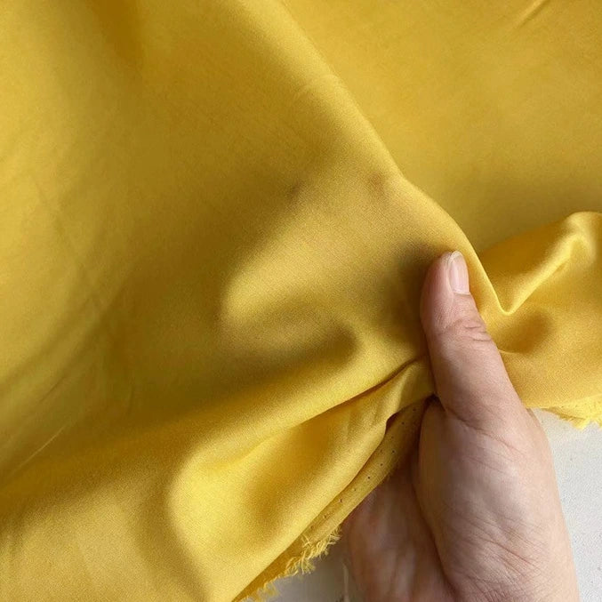 Une main tient un morceau de Soie de coton multicolore au mètre de Longan Craft France, révélant sa texture lisse, son drapé doux et sa nature légère - idéale comme doublure de soie grâce à son mélange de soie de mûrier respirant avec des bords fins.