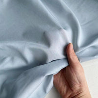 Une main tient et fronce délicatement Soie de coton multicolore au mètre de Longan Craft France, un tissu de doublure en soie de mûrier léger et respirant qui met en valeur sa texture douce et son drapé élégant.