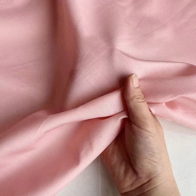 Une main soulève un morceau de Soie de coton multicolore au mètre de Longan Craft France, montrant la texture douce et lisse et le drapé élégant de cette légère soie de mûrier, un tissu de doublure respirant, sur un fond blanc.