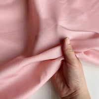Une main soulève un morceau de Soie de coton multicolore au mètre de Longan Craft France, montrant la texture douce et lisse et le drapé élégant de cette légère soie de mûrier, un tissu de doublure respirant, sur un fond blanc.
