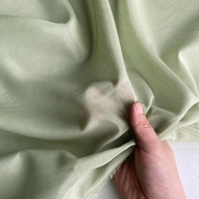 Une main recueille délicatement un morceau de Soie de coton multicolore au mètre de Longan Craft France, mettant en valeur la texture délicate et la gracieuse translucidité de cette légère soie de mûrier, parfaite comme tissu de doublure en soie respirante.