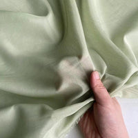 Une main recueille délicatement un morceau de Soie de coton multicolore au mètre de Longan Craft France, mettant en valeur la texture délicate et la gracieuse translucidité de cette légère soie de mûrier, parfaite comme tissu de doublure en soie respirante.